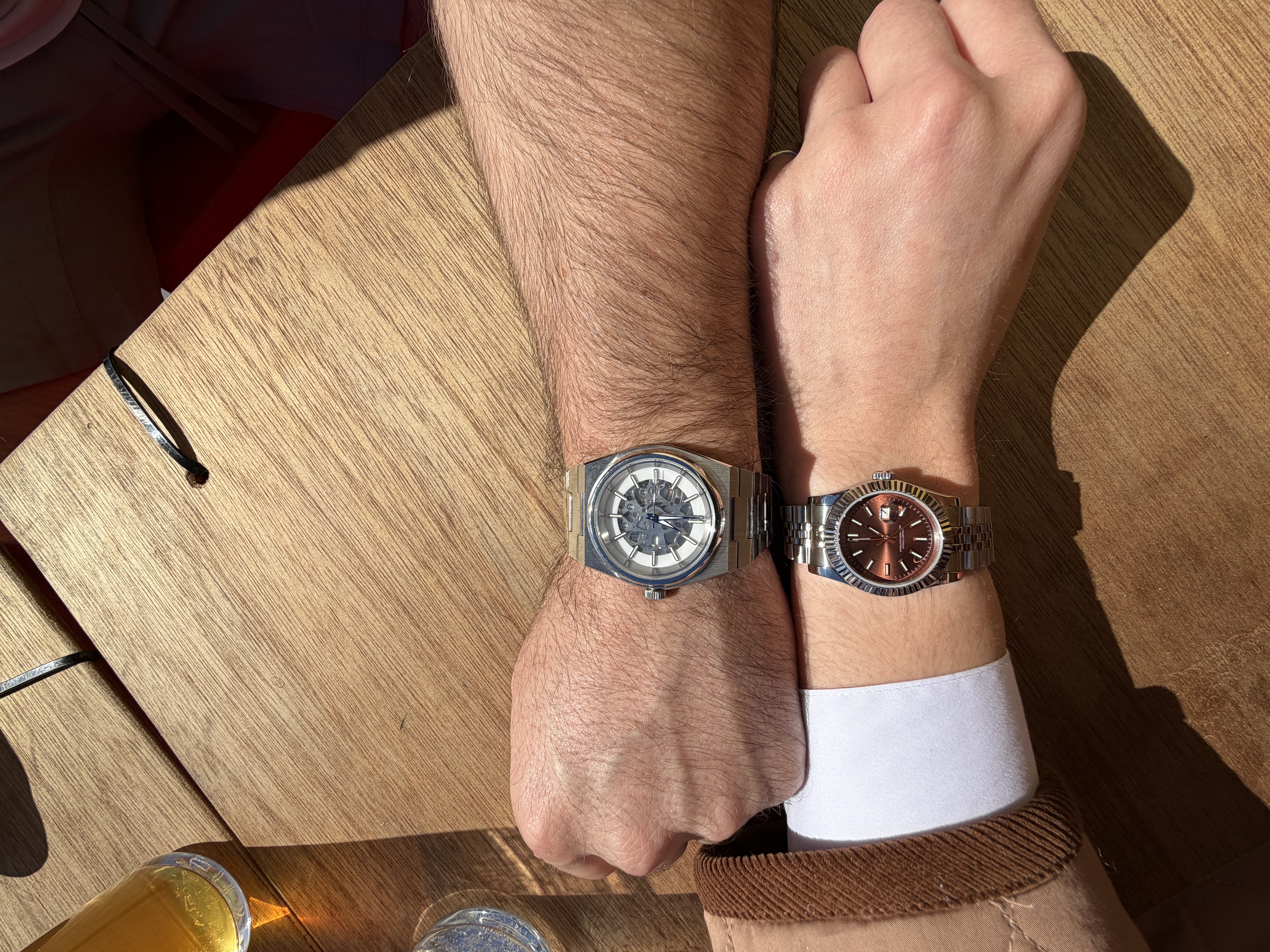 His and hers builds — NH70 skeleton on his wrist, chocolate NH05 Datejust on hers — at a café table